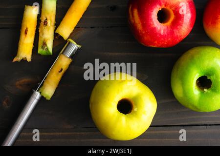 Cored Apples on a Rustic Wooden Table: Ambrosia, Golden Delicious, and Granny Smith apples with a coring tool on a dark background Stock Photo