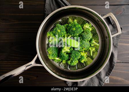 Broccoli Florets on a Steamer Basket Placed in a Saute Pan: Raw broccoli florets in a foldable metal steaming basket placed in a skillet with water Stock Photo