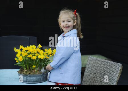 A girl in a dress near a pot of daffodils Stock Photo