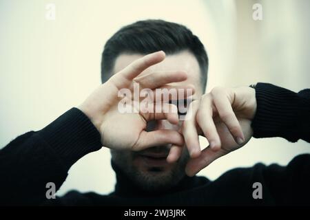 Young man in a dark turtleneck covers his face with his hands in a thoughtful or emotional moment Stock Photo