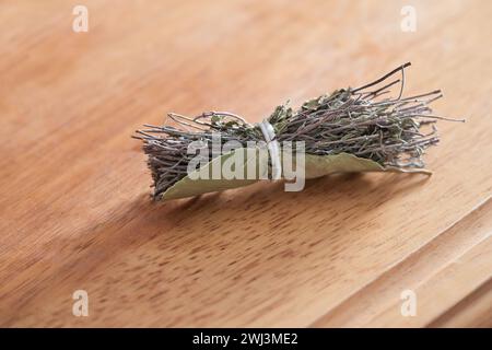 Bouquet garni (French for garnished bouquet) on a wooden board, bundle of dried herbs with thyme, rosemary, marjoram and a bay l Stock Photo