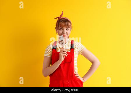 Thoughtful female decorator with paint brush on yellow background Stock Photo