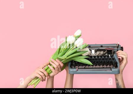 Hands holding vintage typewriter and tulips on pink background. Women's Day celebration Stock Photo
