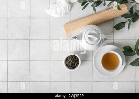 Teapot, cup of tea and bowl with dry leaves on white tile background Stock Photo