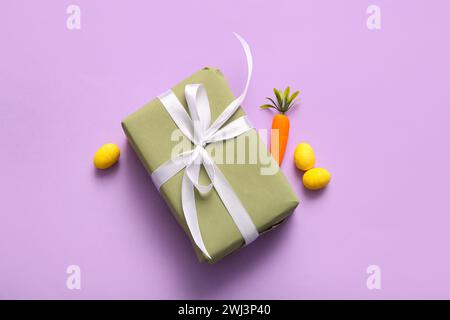 Easter eggs with carrot and gift box on purple background Stock Photo