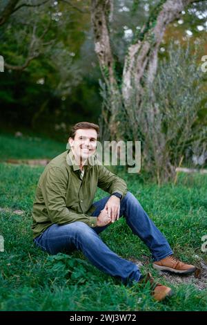 Smiling young man sitting on green grass in the park Stock Photo
