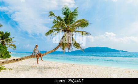 Young woman relaxing at a coconut palm tree on a white tropical beach at La Digue Seychelles Islands Stock Photo
