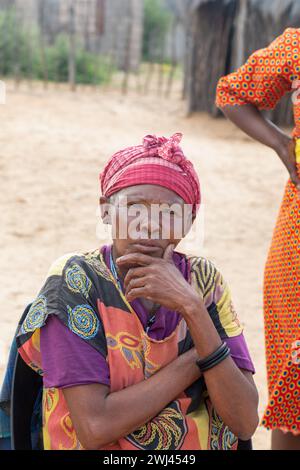 village african old woman portrait, wearing traditional geometric tribal patterns , sited on a chair outside in the yard Stock Photo