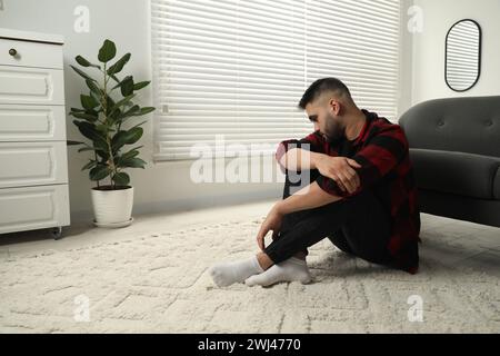 Sad man sitting on floor at home. Space for text Stock Photo