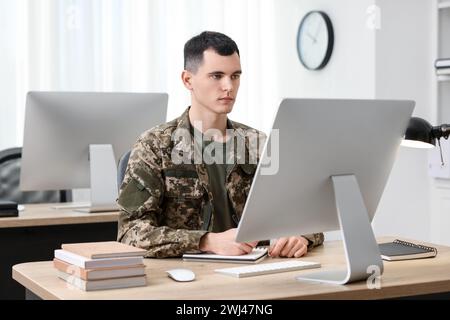 Military education. Young student in soldier uniform learning at wooden table in room Stock Photo