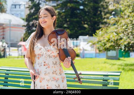 busker latin woman young long haired violinist cute with dress, in park standing calmly with her eyes closed resting and with her violin Stock Photo