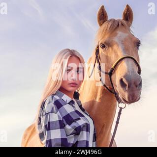 Portrait of a young blonde girl with a beige horse on the ranch close up Stock Photo