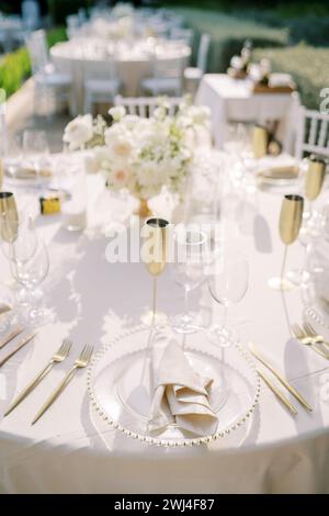Set table with glasses and bronze goblets with a bouquet of flowers stands in the garden Stock Photo