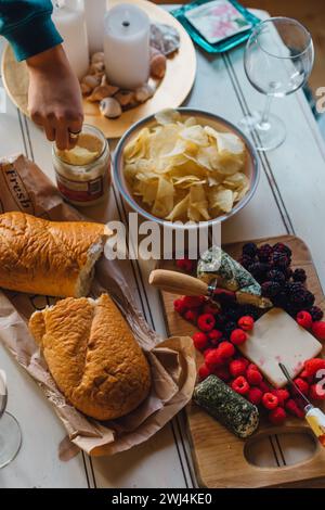 high angle view of snack spread on coffee table with cheese board, berries, chips, bread, dip, empty wine glasses and head dipping chip in jar Stock Photo
