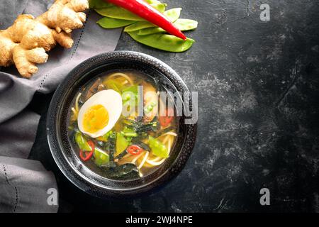 Asia soup with noodles, miso, vegetables, ginger and an egg in a black ceramic bowl on a dark background, high angle view from a Stock Photo