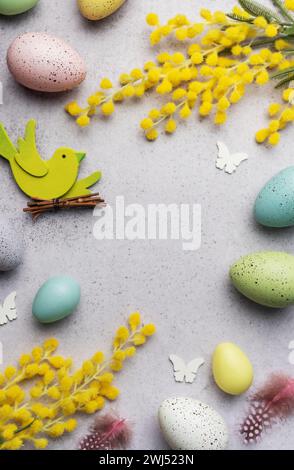 Decorative Easter composition featuring pastel-colored eggs, vibrant mimosa branches, and festive cutouts on a light, textured surface. Stock Photo