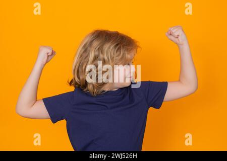 Child showing muscles on yellow studio isolated background. Power kids. Kid showing strong fists. Stock Photo