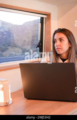 A woman sits in front of her laptop computer, working remotely inside a van looking from the window Stock Photo