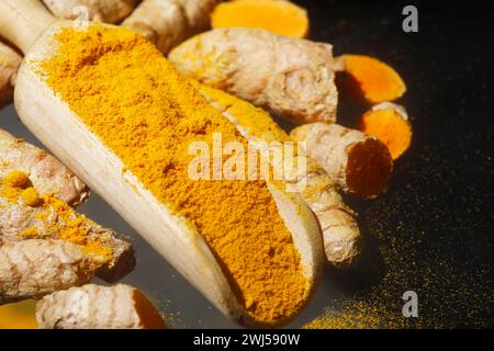 Turmeric powder (Kurkuma) in a wooden spoon and roots Stock Photo