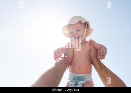 Father's hand lifts a joyful baby against a sunlit sky. Concept of paternal love and playful moments Stock Photo