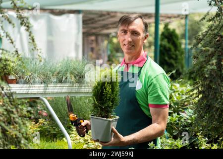 Man working in a garden center standing and holding plants Stock Photo