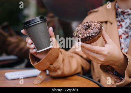 Female hands are holding a donut and a cup of coffee Stock Photo