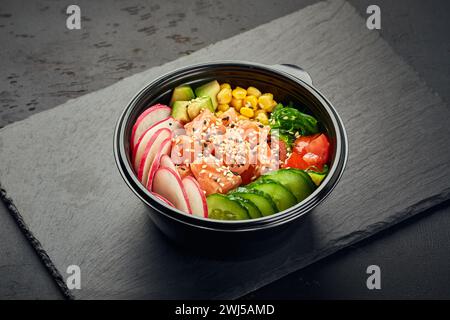 Poke bowl with salmon, avocado, radish, cucumber, tomato, sweet corn and chukka salad in plastic bowl Stock Photo