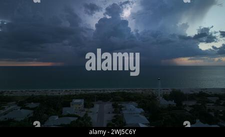 Seashore town with dark houses and lighthouse on ocean shore with blinking light at stormy night for commercial vessels navigation. Thunderstorm with Stock Photo