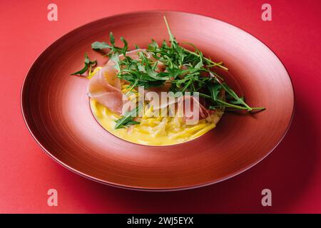 Spaghetti with prosciutto and arugula on red plate Stock Photo