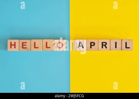 Hello month of April concept. Wooden blocks typography in bright blue and yellow background. Stock Photo