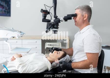 Dentist using dental microscope treating patient teeth at dental clinic office. Medicine, dentistry and health care concept. Den Stock Photo