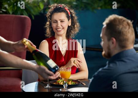 Young couple having dinner in restaurant. Waiter brought a bottle of champagne Stock Photo