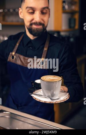 Smiling mature waiter serving hot coffee at cafeteria Stock Photo