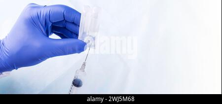 The Medical gloved hands holding syringe with a bead of liquid emerging testing the function of the syringe Stock Photo