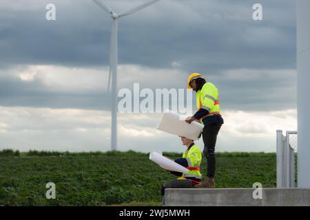 Engineers and technicians work together on the tower base of a large wind turbine with a wind turbine field in the background, T Stock Photo