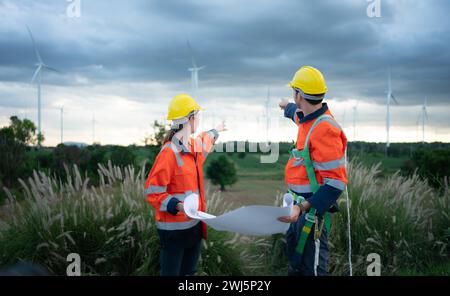 Two engineers working on a construction site with wind turbines in the background Stock Photo