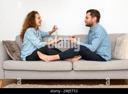 Couple sits on sofa and using one laptop together. Booking online. Internet store and family online shopping. Stock Photo