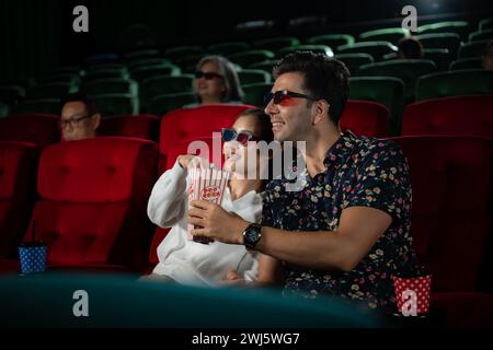 In a cinema, A young couple pair wearing 3D glasses watches movies and eats popcorn. Stock Photo