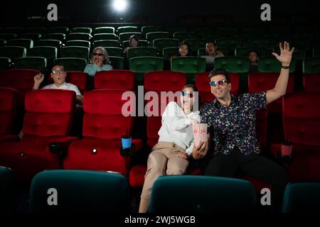 In a cinema, A young couple pair wearing 3D glasses watches movies and eats popcorn. Stock Photo