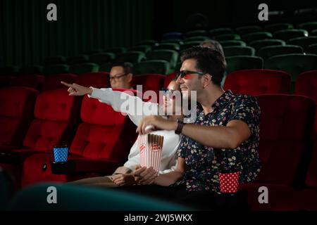 In a cinema, A young couple pair wearing 3D glasses watches movies and eats popcorn. Stock Photo