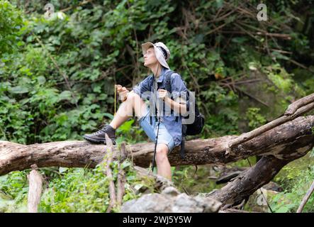 Young man traveler sitting on a fallen tree and looking at the compass in hand. Stock Photo