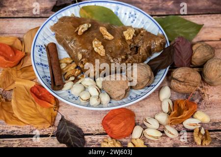 Turkish Baklava sweet cake on the plate, decorated with fresh pistachios, nuts, lemon, apple, vanilla and dry autumn leaves, on wooden massive table Stock Photo