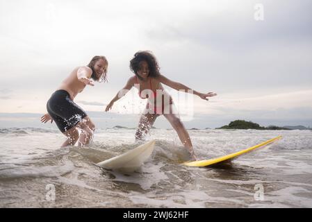 Couple surfing on the beach having fun and balancing on the surfboard Stock Photo