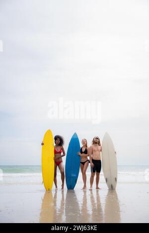 Group of friends in swimsuits posing with surfboards on the beach. Stock Photo