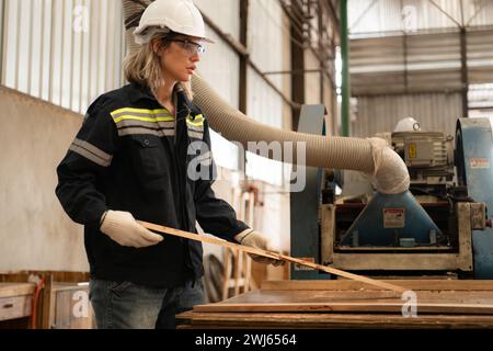 A carpenter works in a carpentry workshop. She collects the wood that passes through the wood angle grinder. Stock Photo