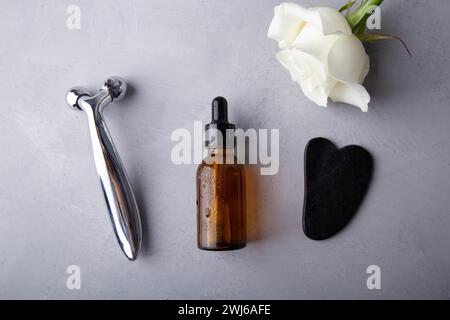 Luxurious skincare routine with a white rose and facial tools on a grey backdrop. Stock Photo
