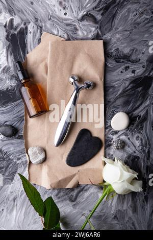 Elegant white rose with massage roller, serum, gua sha and organic skincare. Modern facial care tools with rose and essential oil for beauty routine. Stock Photo