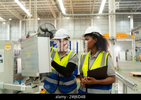 Portrait of two female engineers using laptop while standing in factory, To check the operation of the machine's circuit board. Stock Photo
