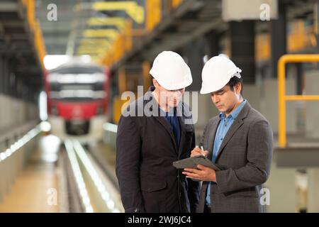 Two businessmen inspect the electric train system using a tablet to reserve equipment for use in repairing tracks and machinery Stock Photo