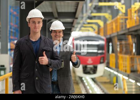 Portrait of two young engineers showing thumbs up in front of train station Stock Photo